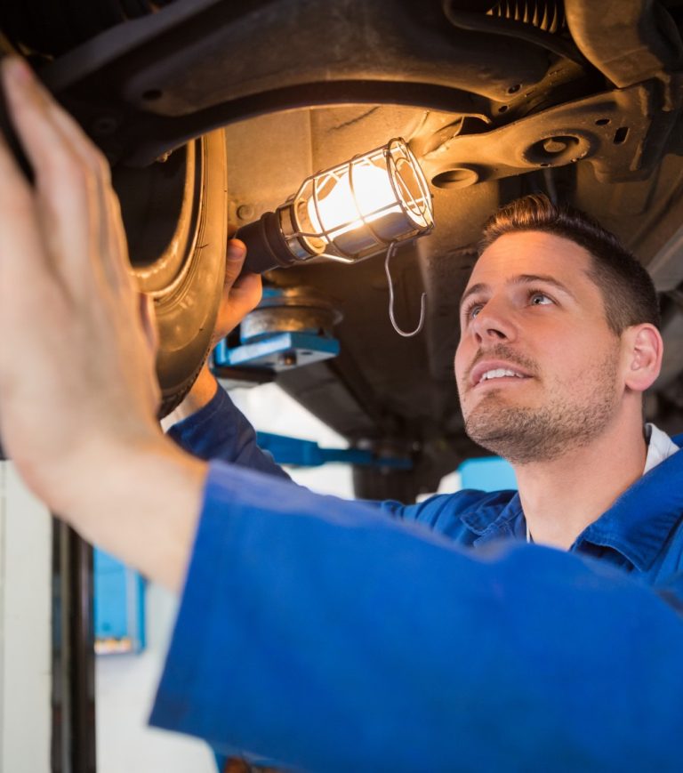 A mechanic in blue overalls inspects a car from underneath during an MOT in Northampton